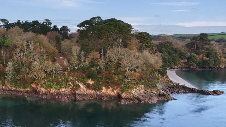 An aerial view of Durgan Wood Cottage peeking through the woodland next to the Helford River, with Grebe Beach nearby, Cornwall